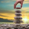 happy-new-year-concept-years-written-rising-stone-pile-man-hand-adding-stone-to-tower-background-blurred-sunset-happy-211638724